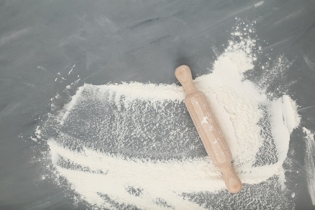 Flour and wooden rolling pin on a gray background, baking ingredients. Top view, copy space.