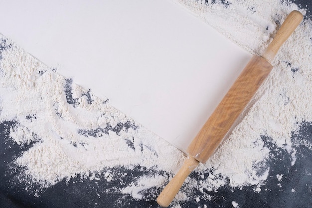 Flour and wooden rolling pin on a gray concrete stone table.