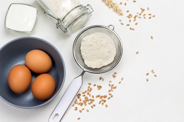 Flour in wooden spoon sieve and glass jar white surface Flat lay