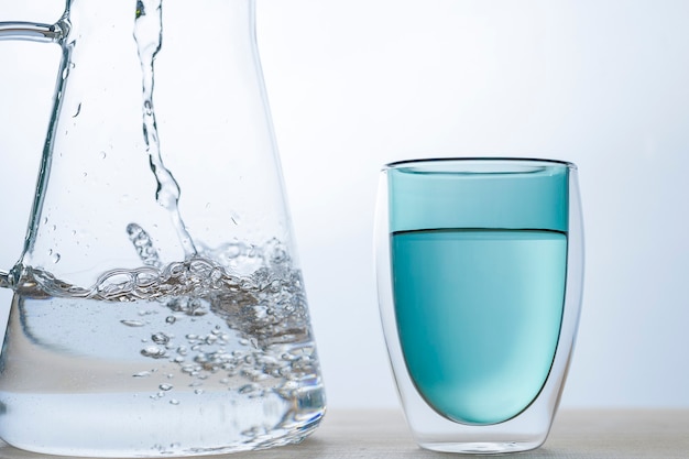 Flow of water is pouring into the green glass on white background.