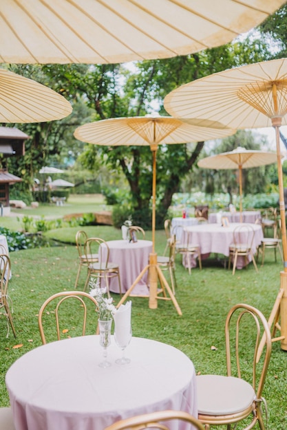 風の強い日にレストランのガラスのディナーテーブルにバラと緑の枝で作られた夏の結婚式のフラワーアレンジメントとフィルムグレイン効果のある屋外のレストランのプレート