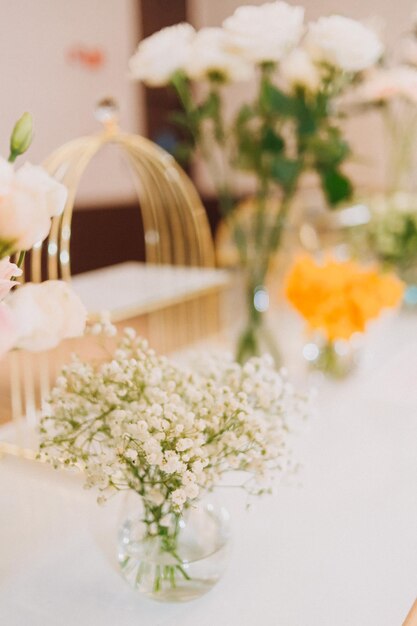 Flower arrangement for summer wedding made of roses and green branches on a dinner table in the restaurant glass and plates in the restaurant outside on a windy day with film grain effect