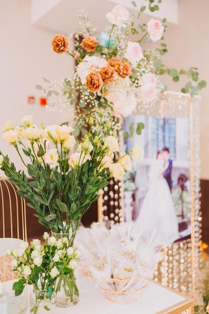 Composizione floreale per il matrimonio estivo fatto di rose e rami verdi su un tavolo da pranzo nel ristorante vetro e piatti nel ristorante all'aperto in una giornata ventosa con effetto grana della pellicola