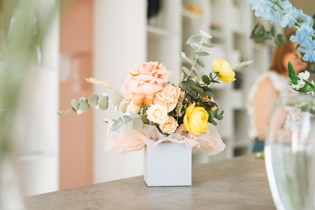 Flower arrangement with yellow and pink roses and eucalyptus in gift box on table in flower shop