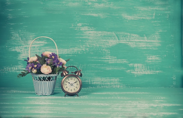 Photo flower in basket with clock on wood background.