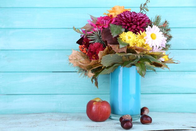 Flower bouquet in blue vase and apple on table on blue wooden wall background