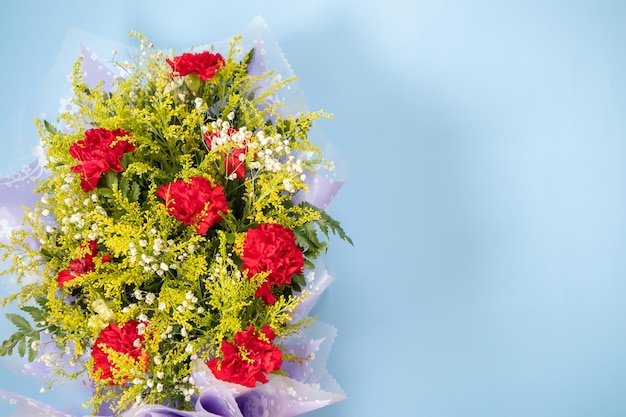 Flower bouquet of red carnation with green leaves on blue background