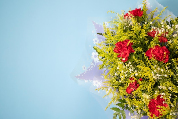 青の背景に緑の葉と赤いカーネーションの花の花束