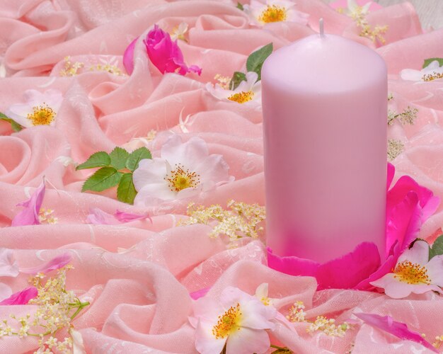 Flower composition of white and pink flowers and a pink candle\
on pink cloth