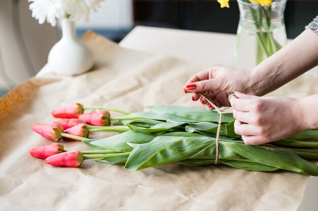 花の配達。赤いチューリップの花束をアレンジする花屋。女性の手はより糸の弓を結びます。