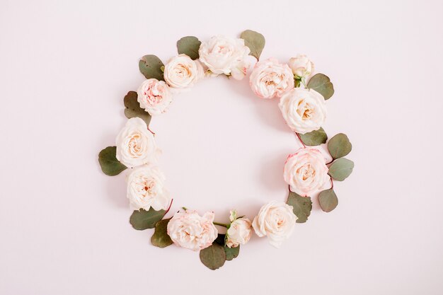 Flower frame made of beige roses, eucalyptus branches on pale pastel pink background. Flat lay, top view