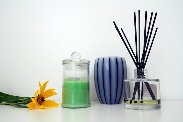 Flower of Jerusalem artichoke Scented candles on a white background Aromatic sticks soaked in essential oil Glass vessel with oil Still life Striped candle wax in a transparent jar with a lid