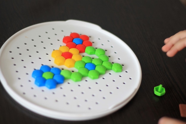 A flower made from plastic beads is on a table with a green and orange flower