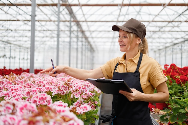 Flower nursery female worker with clipboard taking inventory of flowers