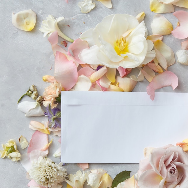 Лепестки цветов с белым конвертом и местом для текста на бетонном фоне, плоская планировка