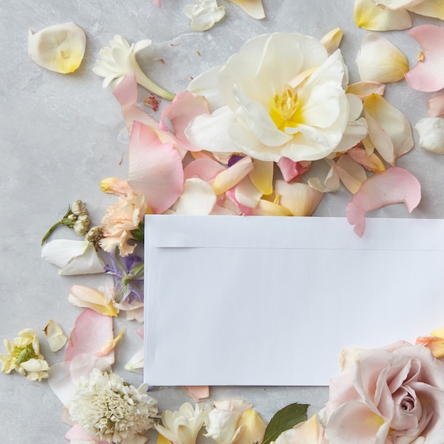 Foto petali di fiori con una busta bianca e posto per il testo su uno sfondo di cemento, piatto