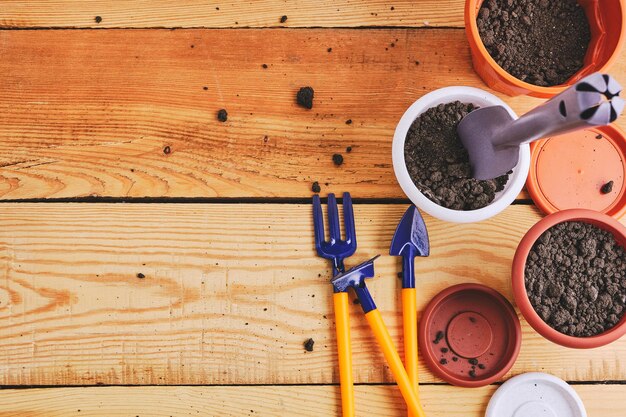 Photo flower pots and set decorative gardening tools shovel rake and pitchfork on a wooden background