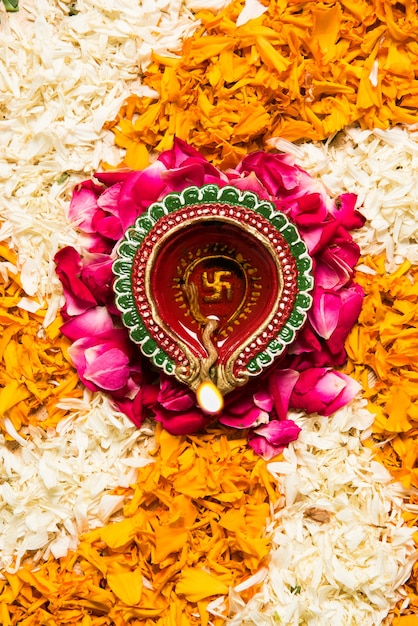 Flower rangoli for Diwali or Pongal made using marigold or zendu flowers and red rose petals over white background with Clay Oil Lamp in the middle, selective focus