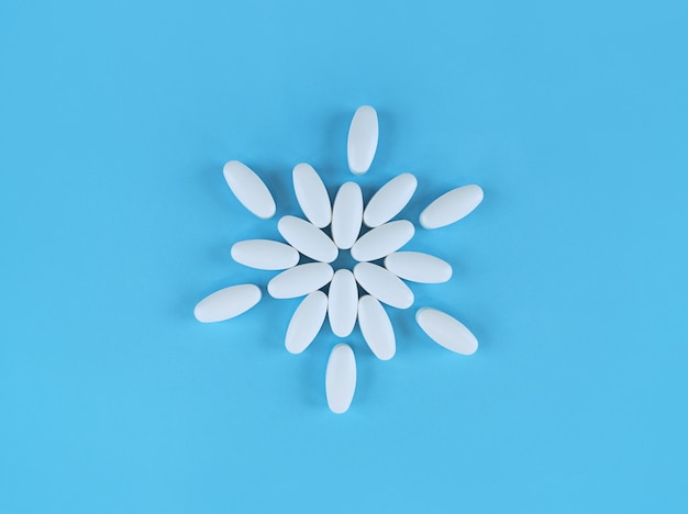 Flower shape made from white tablets on blue, flat lay