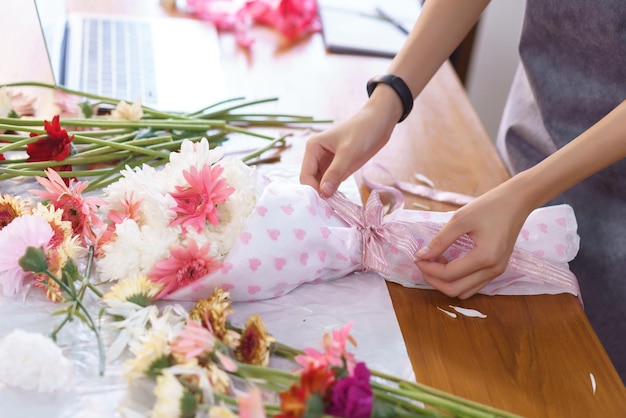 フラワー ショップのコンセプト 紙とリボンの弓で色とりどりの花の花束を作成する女性の花屋