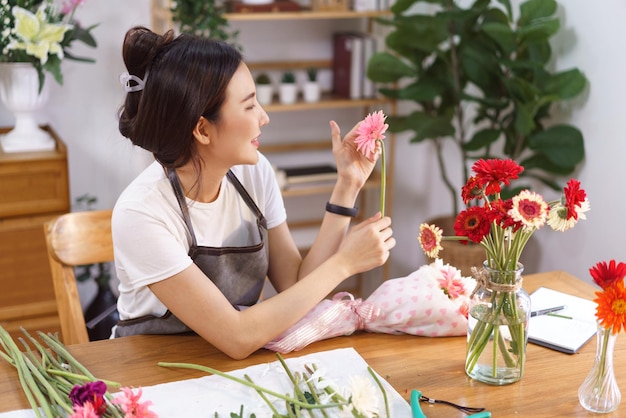 Flower shop concept Female florist holding pink gerbera to decorating in colorful flowers vase