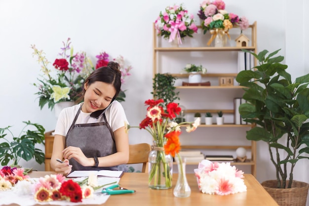 Flower shop concept Female florist holds phone between face and shoulder to talking with customer