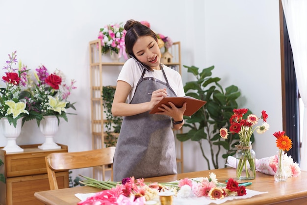Концепция цветочного магазина Женщина-флорист держит телефон между лицом и плечом, чтобы поговорить с покупателем