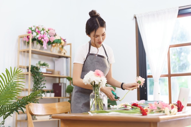 Flower shop concept female florist trim stems of pink gerbera by scissor for arranging in vase