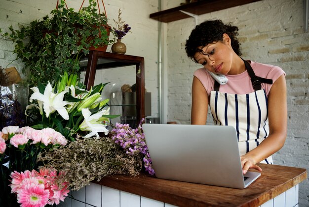 Proprietario del negozio di fiori che parla sul telefono facendo uso del computer portatile del computer