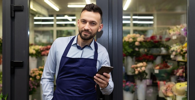 The flower shop salesman is talking on the phone next to the refrigerator with flowers