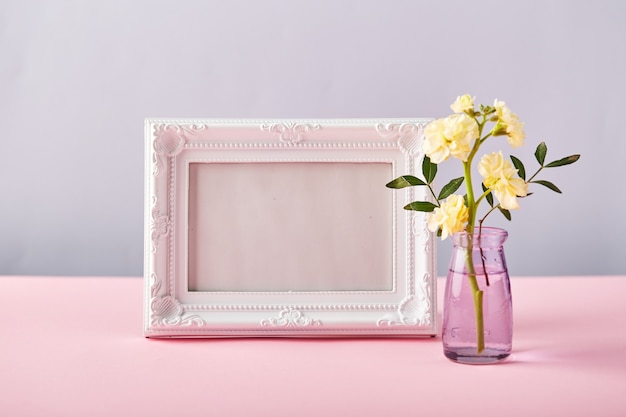 Flower of yellow matthiola in little glass vase with white photo frame on pink table