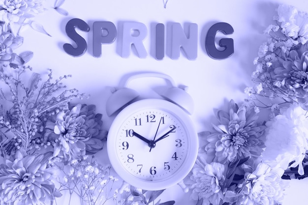 Flowers, alarm clock and inscription spring on very peri color trend 2022background top view waiting for spring concept