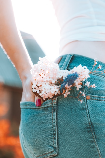 Flowers in the back pocket of blue jeans, a girl with red manicure