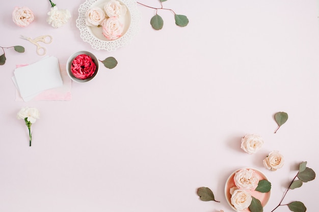 Flowers border frame made of beige and red roses and white carnation on pale pastel pink background. Flat lay, top view