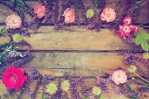 Цветы в кругу на деревянном фоне Открытка к празднику Розы, герань, лаванда, шалфей и мохнатые каштаны размещены по краям на темных досках.