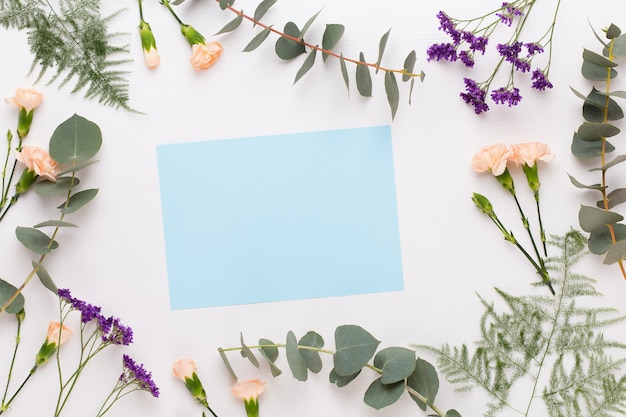 Photo flowers composition. paper blank, carnation flowers, eucalyptus branches on pastel  background. flat lay, top view, copy space