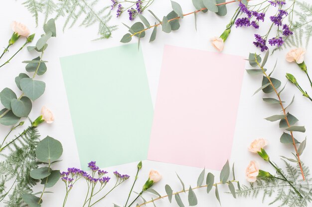 Flowers composition. Paper blank, carnation flowers, eucalyptus branches on pastel  background. Flat lay, top view.