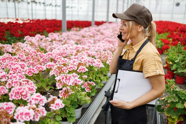 クリップボードで電話で話している花の温室労働者