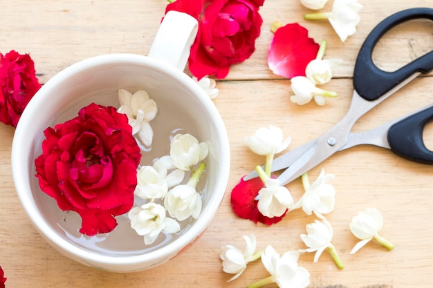 цветы жасминовой розы плавают в чашке с ножницами на деревянном фоне