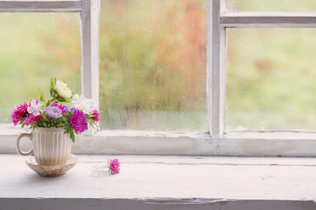 Photo flowers in little cup on old white windowsill