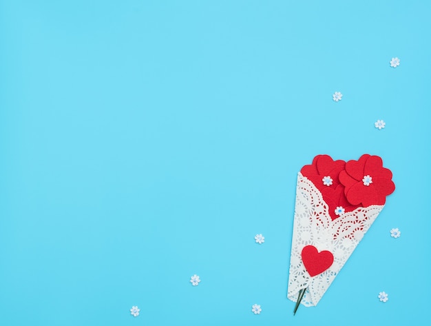 The flowers made of felt hearts wrapped in a white lace bundle on blue background