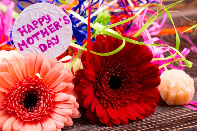 Flowers near Mother's day card. Candy and colorful streamer. Bright gift for mommy. Attention and grattitute on holiday.