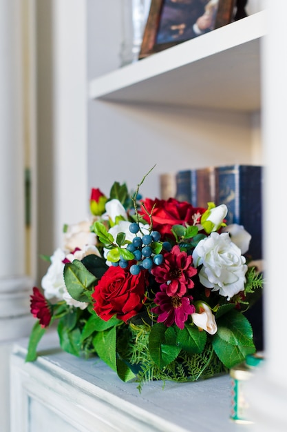 Flowers in an old vase on the shelf with books