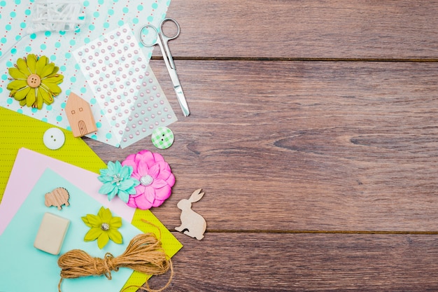 Flowers; paper; pearls; button and thread with scissor on wooden table