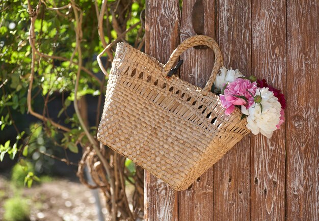 Flowers of pink red and white peonies in wicker basket on wooden table against wooden background