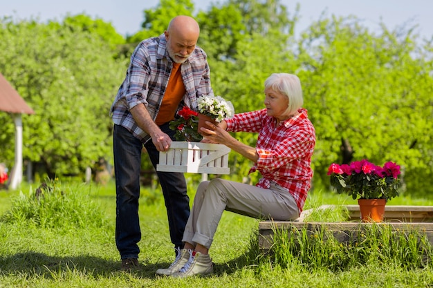 Горшки для цветов. занятые муж и жена на пенсии кладут цветочные горшки в белый ящик, проводят время на улице