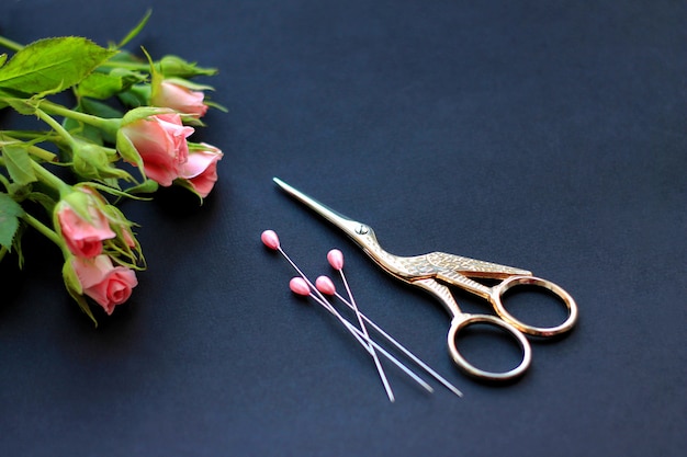 flowers, scissors for sewing and pins on a dark background the concept of congratulations on the holiday and needlework