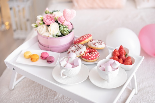 Flowers and sweets on white table and balloons on the white bed. Gift for Mother's Day