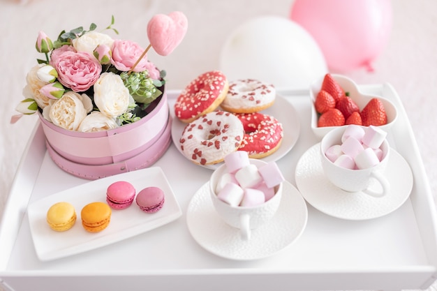 Flowers and sweets on white table and balloons on the white bed. Gift for Mother's Day