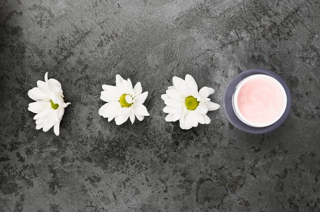 Flowers with a jar of cream on a dark marble surface.